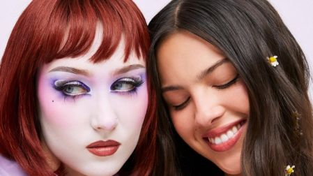 Chappell Roan con cabello rojo y maquillaje morado posa junto a Olivia Rodrigo, sonriente y con flores blancas en el cabello.