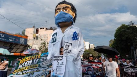 Marcha de trabajadores del IMSS y agremiados del SNTSS exigiendo un salario digno, acompañados de una figura gigante de un trabajador de la salud con cubrebocas.