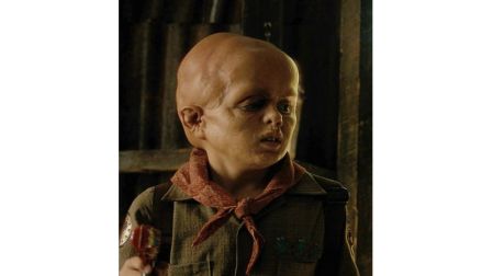 Jason Voorhees de niño en Crystal Lake, con cabeza calva, rostro deformado, uniforme de campamento y pañuelo rojo.