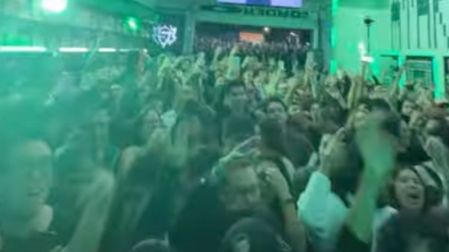Multitud de fans con las manos levantadas bajo luces verdes durante el minishow de Martin Garrix en una taquería de CDMX.