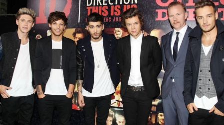 Integrantes de One Direction, incluido Liam Payne a la derecha, posan junto a un hombre de traje ante un cartel de la banda.