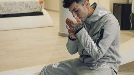 Naim Darrechi viste sudadera y pantalón deportivos grises de Nike, sentado con las manos juntas y tatuajes visibles.
