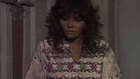 Verónica Castro con cabello rizado y blusa bordada frente a una puerta en una escena de Los ricos también lloran.