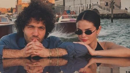 Selena Gomez con lentes oscuros y Benny Blanco con camisa azul posan juntos en una embarcación en Venecia.