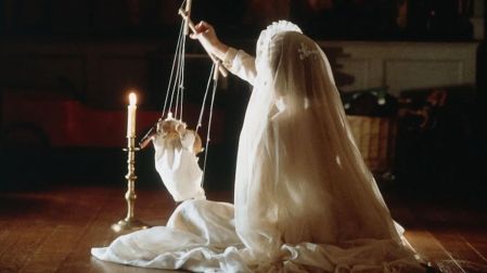 Escena de Los otros con una figura cubierta por un velo blanco que sostiene una marioneta junto a una vela encendida.