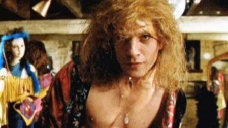 Ted Levine como Buffalo Bill en El silencio de los inocentes, con peluca rubia, collar y bata abierta frente a la cámara.