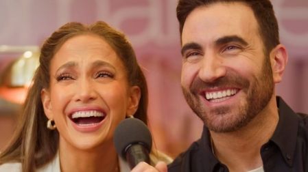 Jennifer Lopez y Brett Goldstein sonríen durante una entrevista con micrófono sobre Office Romance, en medio de rumores de romance.