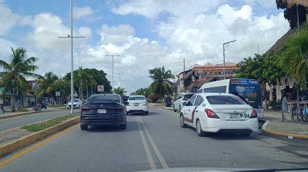 Taxi local color blanco circulando por una avenida principal con tráfico en Tulum, Quintana Roo.