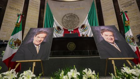 Fotografías de Francisco Garfias, rodeadas de flores blancas, flanquean la tribuna del Salón de Plenos durante el homenaje en la Cámara de Diputados.