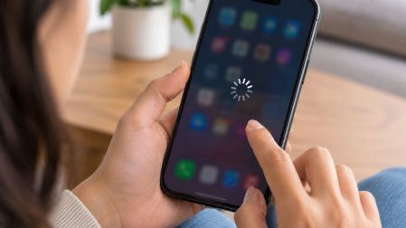 Persona intenta utilizar un celular con la pantalla congelada y un símbolo de carga sobre los iconos de aplicaciones.