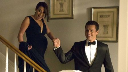 Lea Michele embarazada como Rachel Berry, con vestido negro, baja una escalera tomada de la mano de Jonathan Groff en Glee.