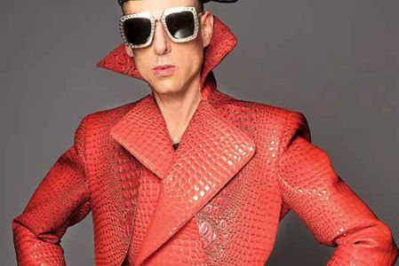 Edy Smol viste un traje rojo con textura de piel de reptil, gafas de sol con diamantes y sombrero negro, mostrando su estilo audaz y su influencia en la moda.