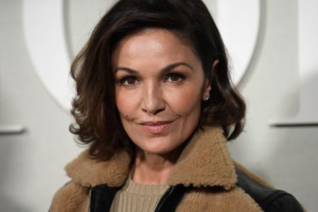 La actriz francesa Nadia Farès posa en primer plano durante un evento de moda en París, con chaqueta oscura y fondo desenfocado.