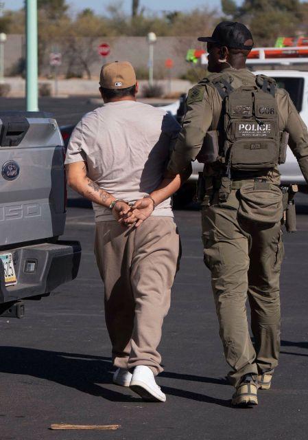 Un inmigrante documentado detenido por el Servicio de Inmigración y Control de Aduanas de Estados Unidos (ICE), camina esposado mientras un agente lo sujeta del brazo en el estacionamiento de un Home Depot en Tucson, Arizona.