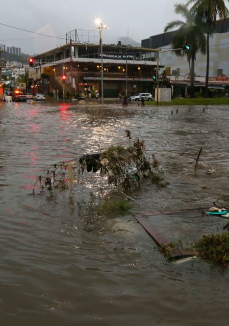 Ramas, basura y escombros flotando en una intersección vial inundada en Acapulco, cerca de una plaza comercial.