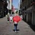 Una persona caminando por una calle peatonal de tiendas en Nantes, sosteniendo un paraguas rojo abierto como parasol para protegerse del sol abrasador.