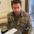 Hugh Jackman caracterizado como Wolverine, con barba y camisa a cuadros, sentado frente a una mesa con comida.