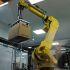 Brazo robótico industrial manipula una caja marcada como frágil dentro de una planta farmacéutica, representando la automatización de procesos, la innovación tecnológica y los estándares de seguridad en la producción de medicamentos.