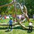 Personas y niños interactúan con una gran escultura de bronce de Molly Gochman en un parque, parte de la serie Monumentos a la Maternidad, una instalación participativa que invita al juego, al contacto físico y a la reflexión sobre el cuidado y la comunidad.