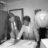 Gladys West, matemática estadounidense y pionera del GPS, revisa mapas y documentos técnicos junto a un colega en una oficina, con globos terráqueos y material cartográfico al fondo.
