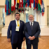 Pedro Haces Barba posa junto a representante internacional en sede de la OEA en Washington, bajo banderas de países miembros durante agenda sobre democracia.
