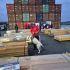 Funcionarios de Aduanas de Chile y un perro detector inspeccionan paquetes de madera en un puerto durante un operativo antidrogas.