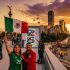 Pareja de aficionados celebrando con la bandera de México frente al Ángel de la Independencia y un letrero del Mundial 2026 al atardecer en la Ciudad de México.