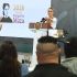 Claudia Sheinbaum, Presidenta de México, preside una conferencia matutina en Tulum, Quintana Roo, con una pantalla al fondo que dice '2026, año de Margarita Maza'. Reporteros con las manos levantadas al frente