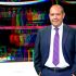 Retrato del periodista Alejandro Leyva Aguilar vistiendo traje oscuro y corbata morada sobre un fondo abstracto de colores.