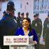 Clara Brugada habla ante un podio durante un informe de seguridad de la Ciudad de México, acompañada por imágenes de policías.