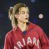 Jimin de BTS con sudadera roja, cabello rubio recogido y audífono de escenario durante un concierto.