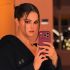 Selena Gomez se toma una selfie frente al espejo con un celular morado, bata negra y cabello recogido.