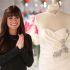 Lea Michele como Rachel Berry en Glee, sonriente junto a un vestido de novia blanco con pedrería y collar de perlas.