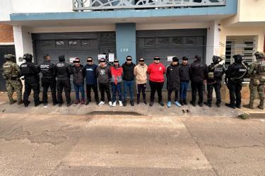Fila de hombres presuntos miembros del CJNG, detenidos y custodiados por elementos de fuerzas especiales frente a una vivienda asegurada.