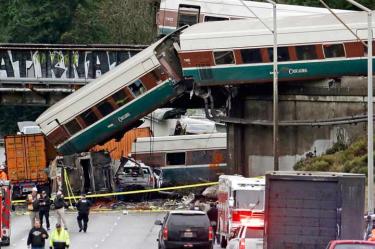 Vagones de un tren Amtrak se ven caídos sobre la Interestatal cinco, junto a varios vehículos destrozados, con algunos vagones aún en las vías más arriba