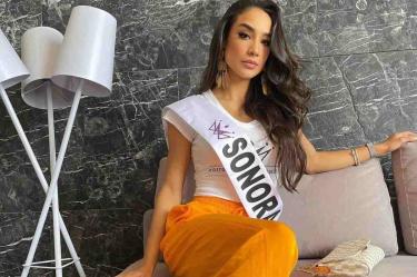 Miss Sonora sentada posando para la foto con blusa blanca y pantalon naranja
