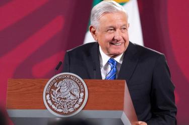 AMLO con traje y corbata sonriendo en su conferencia de hoy