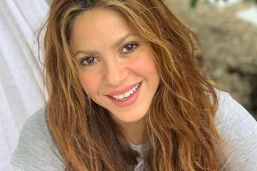 Shakira sonriendo en hamaca, usa playera blanca y cabello suelto
