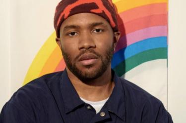 Frank Ocean con gorro y chamarra azul; arcoíris atrás