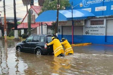 Elementos de bomberos y protección civil empujan un vehículo que quedó atrapado en una inundación