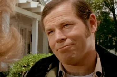 Charles Cyphers sonriendo con chamarra de sheriff