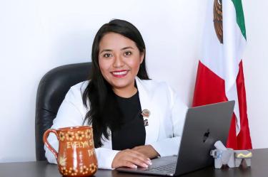 La diputada Evelyn Sánchez posa en su oficina junto a una laptop y la bandera de México durante actividades legislativas.
