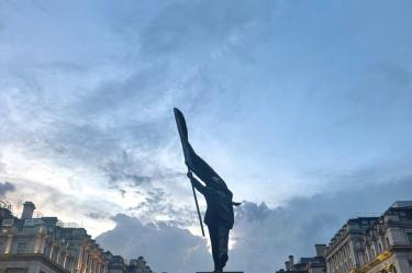 En la escultura, la bandera cubre el rostro del hombre que camina, como una crítica al autoritarismo.