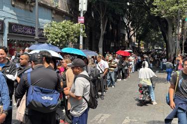 Largas filas de personas esperando pasar por un acceso estrecho hacia el Zócalo de la CDMX, debido a los bloqueos con vallas metálicas de la policía por el plantón de la CNTE.