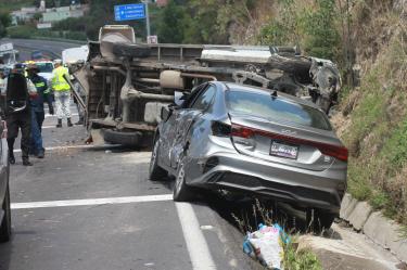 Automóvil sedán gris chocado y camioneta de carga volcada sobre la cinta asfáltica tras un choque múltiple en la carretera Apizaco-Tlaxcala, a la altura del letrero a Tizatlán. Elementos de la Guardia Nacional resguardan el área.