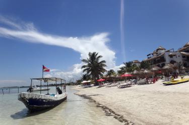 Lancha tradicional anclada en la playa de arena blanca y aguas cristalinas de Mahahual, Quintana Roo, rodeada de palmeras y hoteles boutique.