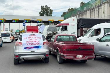 Vehículos particulares y camiones de carga bloqueando una caseta de cobro en Ecatepec con una lona de protesta de la AMOTAC.