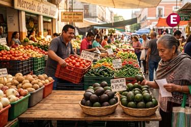 ista de un concurrido mercado al aire libre de México con letreros de precios. Una mujer mayor revisa un aguacate en primer plano con un cartel que dice 'Aguacate $75.00/Kg'. Al fondo, un vendedor sonríe frente a guacales de jitomates rojos ('Jitomate $15.00/Kg') y chiles serranos ('Chile Serrano $20.00/Kg'), ilustrando el costo real de los productos básicos reportados en el informe de inflación del Inegi