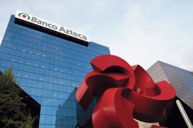Vista del edificio corporativo de Banco Azteca con su logotipo en la parte superior y una escultura roja en primer plano.