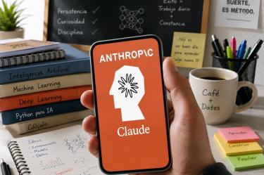 Teléfono móvil muestra el logotipo de Anthropic y Claude sobre un escritorio con libros y apuntes relacionados con inteligencia artificial.